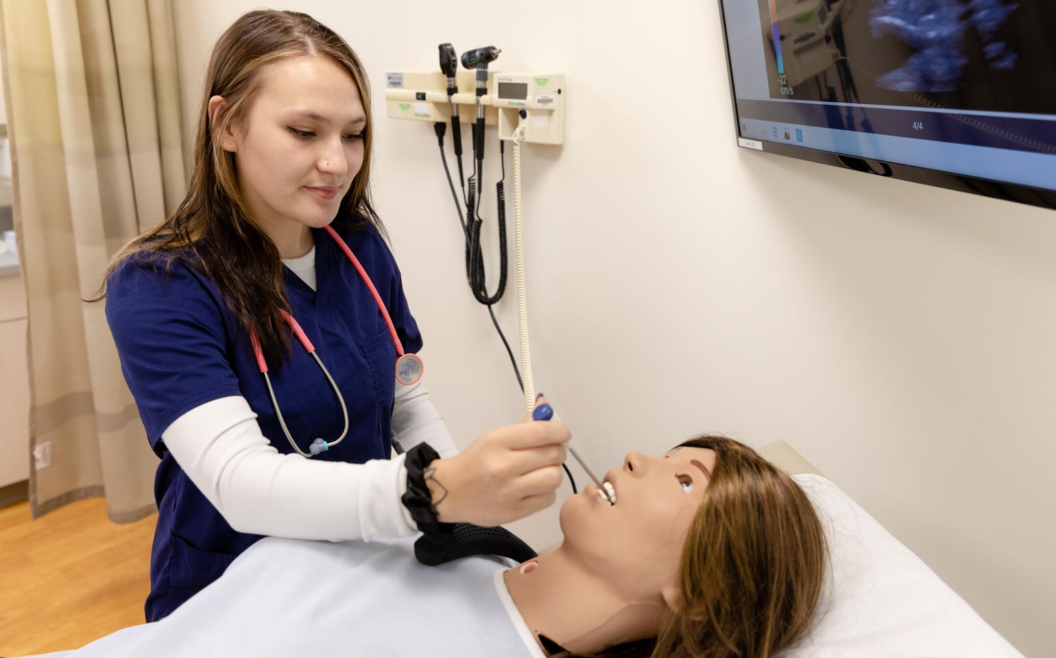 A Nursing student works with a simulated patient in a hospital room.