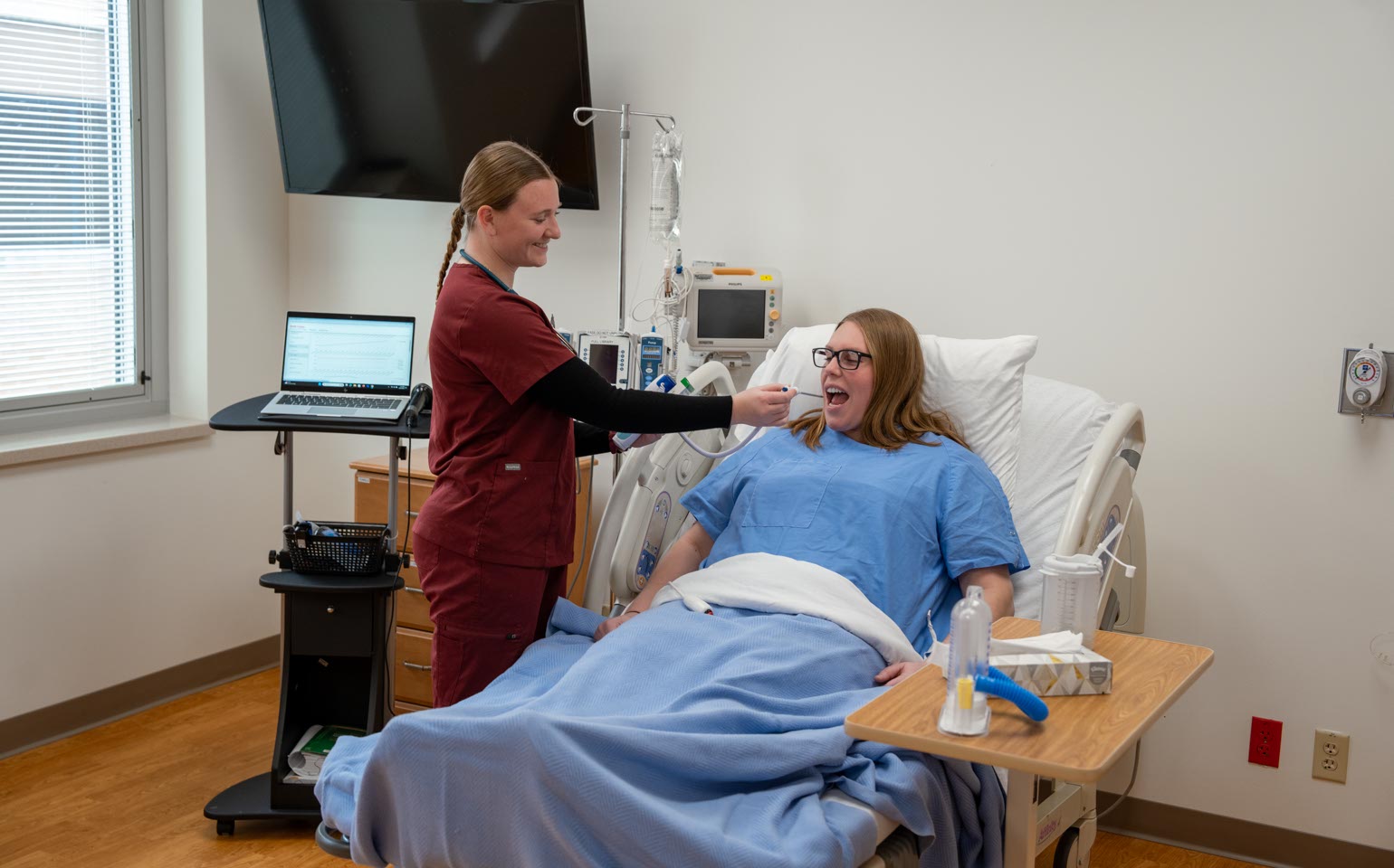 A Nursing student takes the temperature of a patient in a hospital bed.