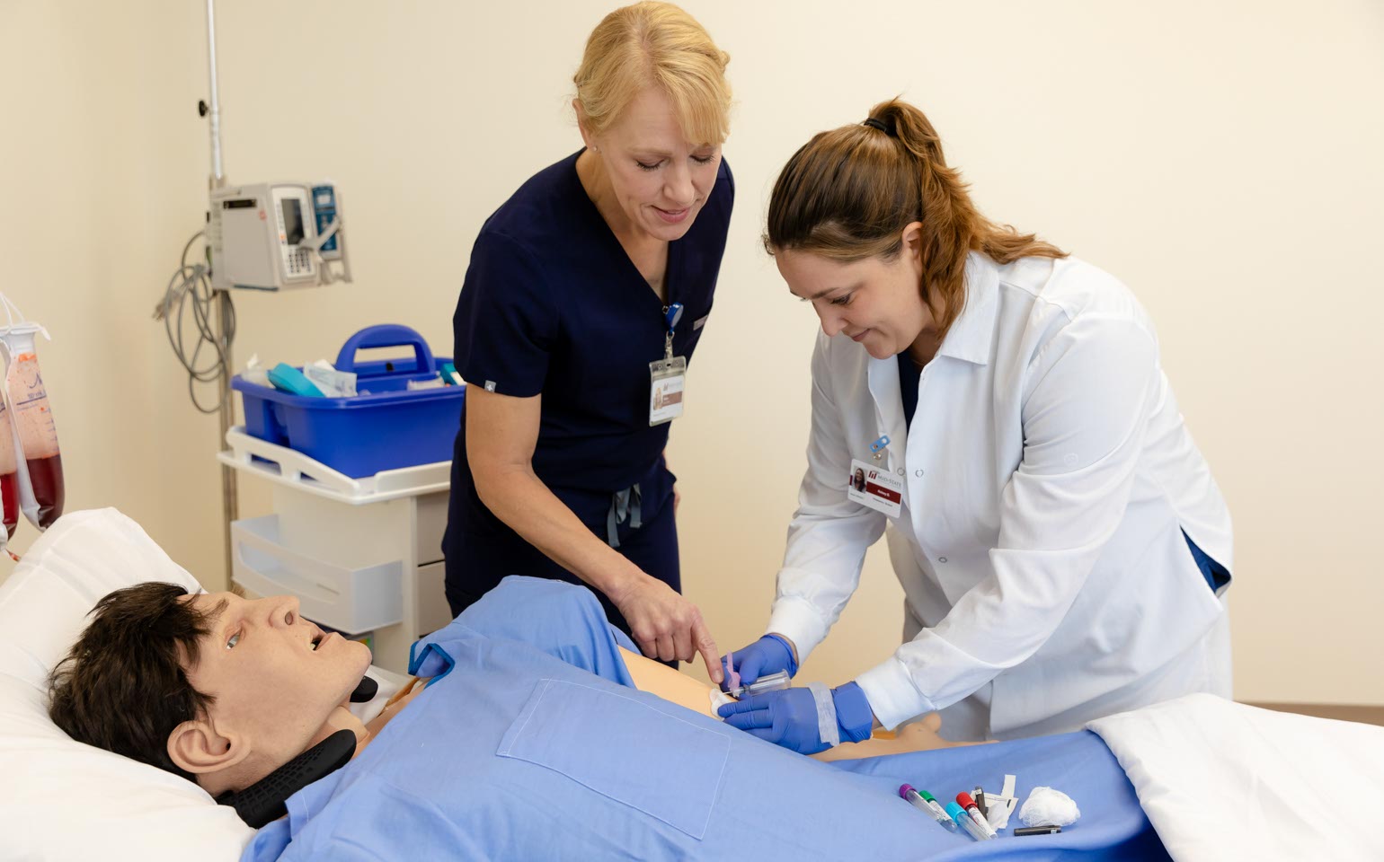 A Phlebotomy Technician assists a student during hands-on practice with a simulated patient.