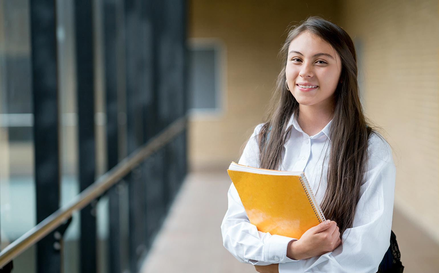 A student smiling at the camera and holding a notebook. 